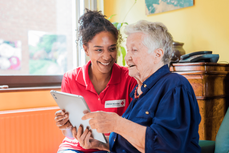 Une bénévole aidant une personne agée à utiliser une tablette