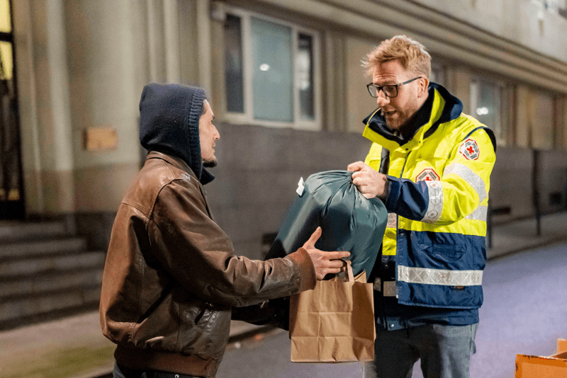 un volontaire qui tend un sac de couchage à une personne sans abris